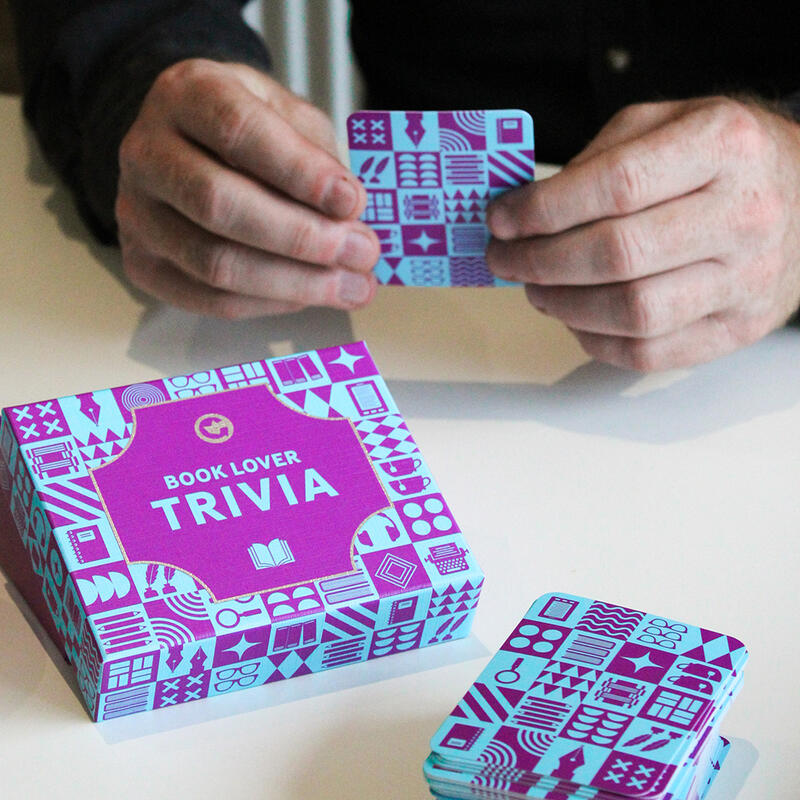close up of the box and question cards with a player reading a question across the table